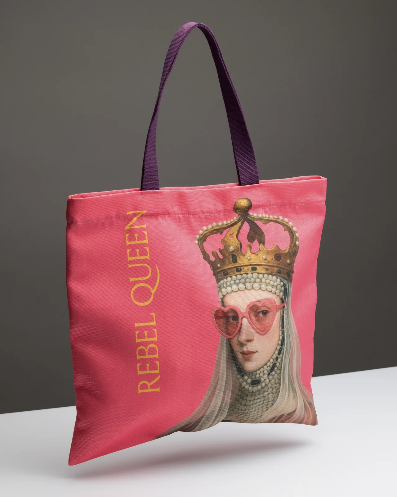 Rožinis krepšys „Rebel Queen“ su violetinėmis rankenomis stovi ant balto paviršiaus