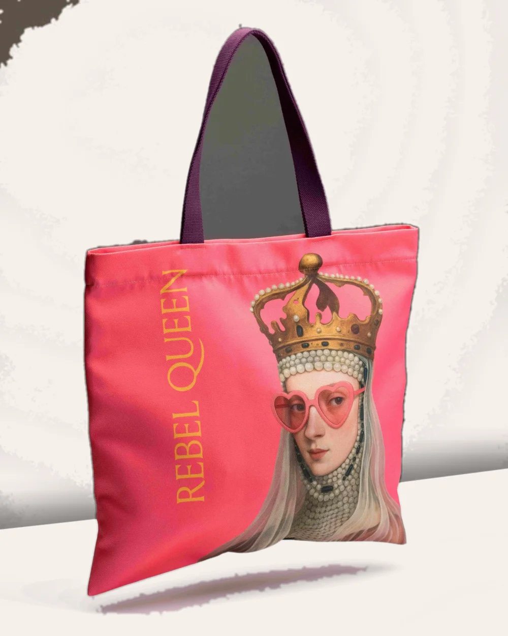 Rožinis krepšys „Rebel Queen“ su violetinėmis rankenomis stovi ant balto paviršiaus