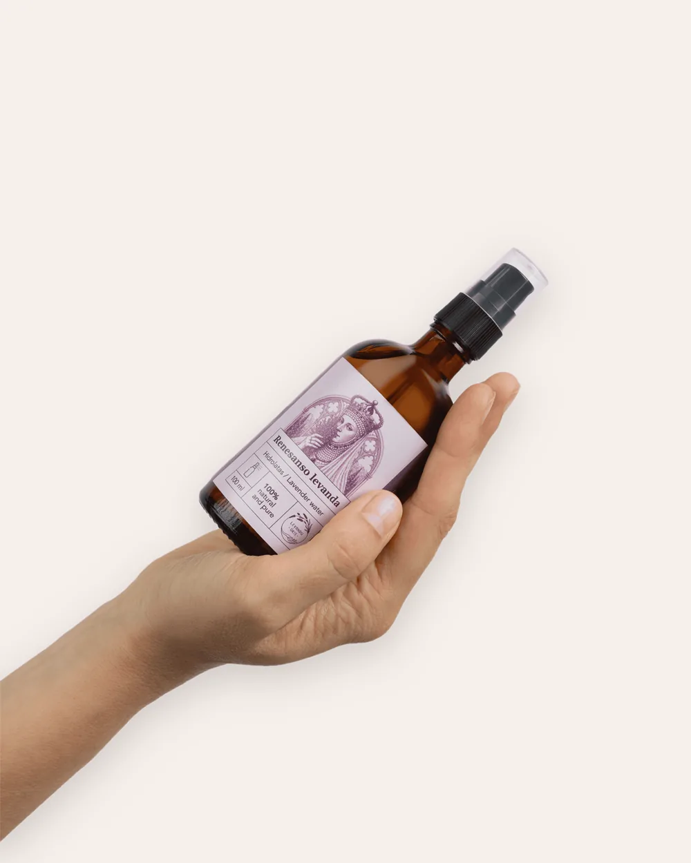 A brown glass spray bottle of “Renaissance Lavender” lavender hydrosol held diagonally in a hand