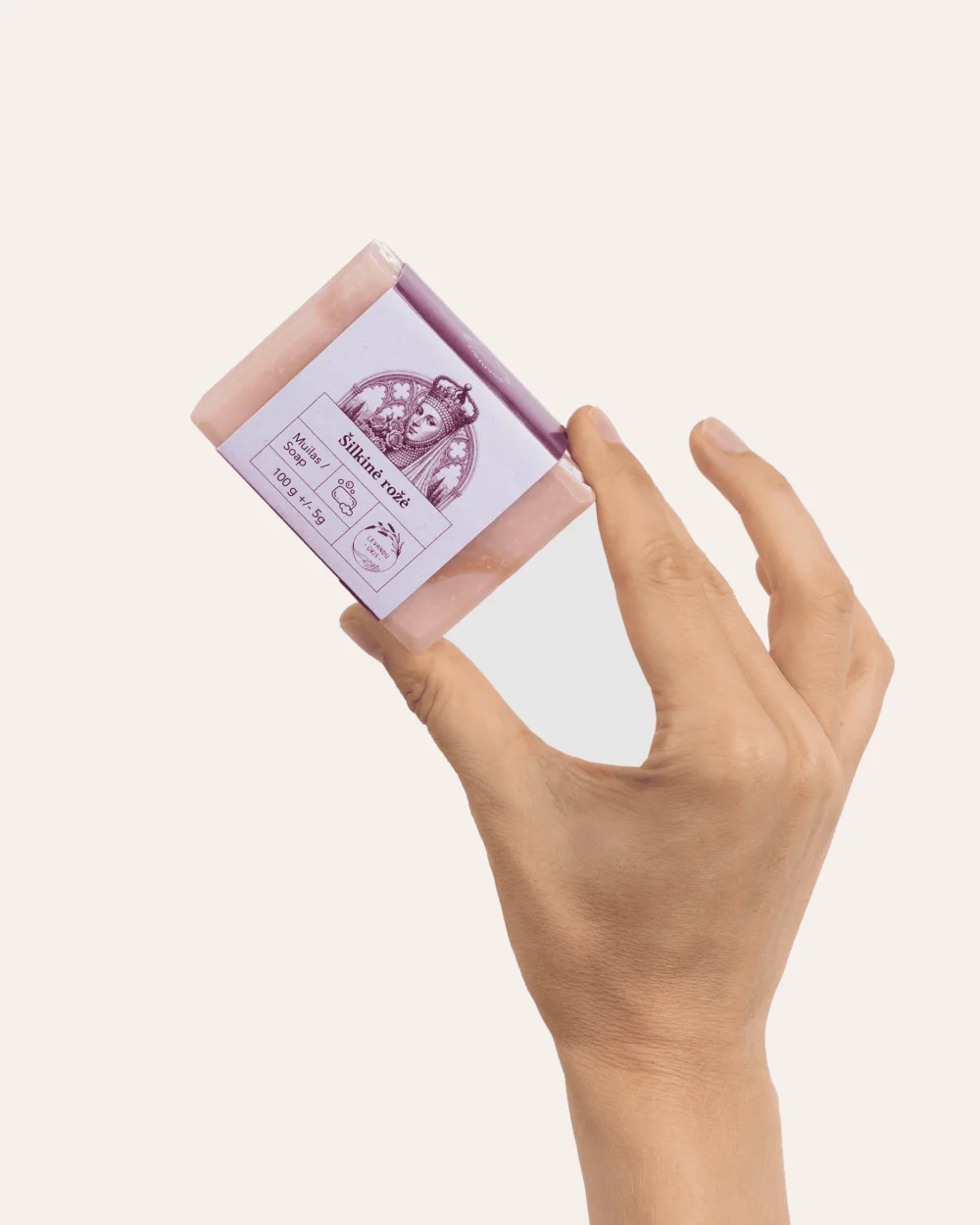 Ranka laiko rausvą kieto muilo „Šilkinė rožė“ 100 g gabalą su etikete, vaizdas kampu