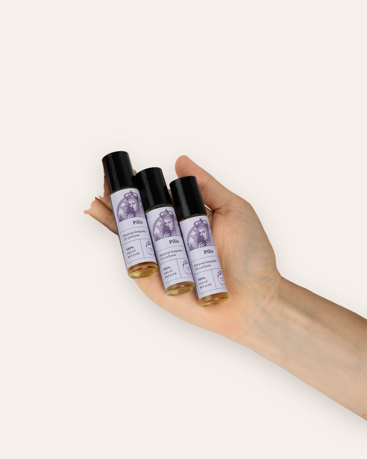 Hand holding three bottles of “The Castle” oil perfume with purple labels