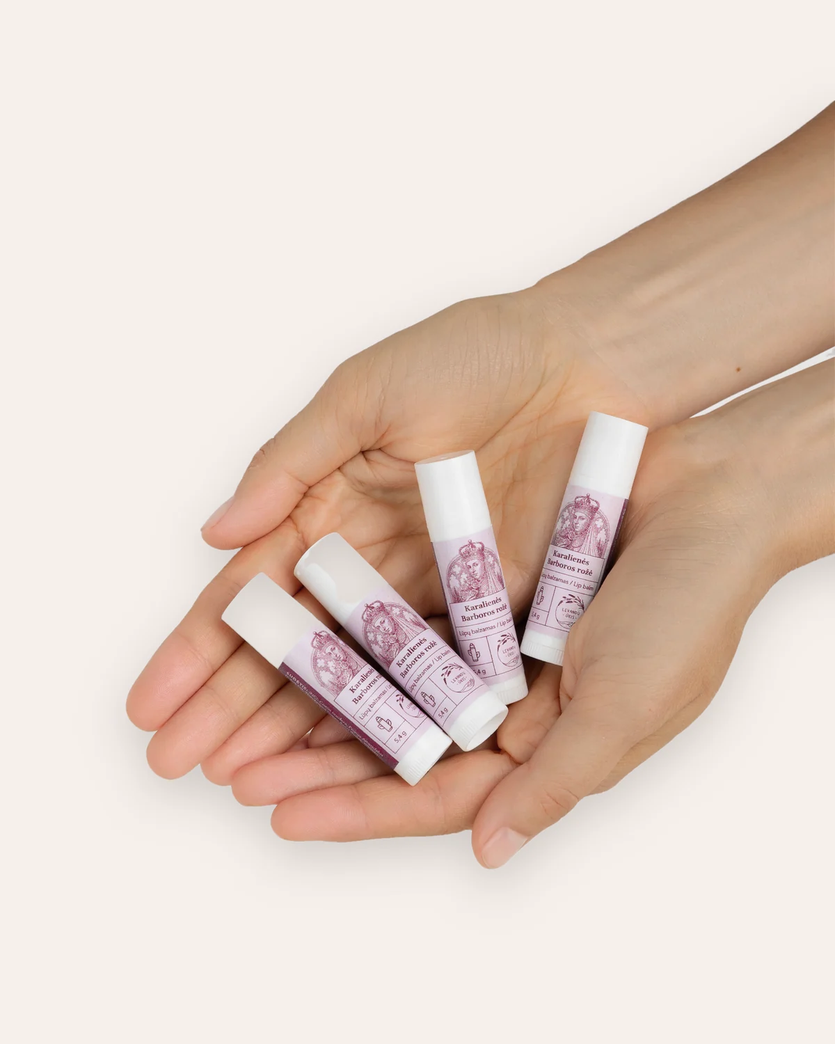 Four “Queen Barbara's Rose” lip balms placed in cupped hands