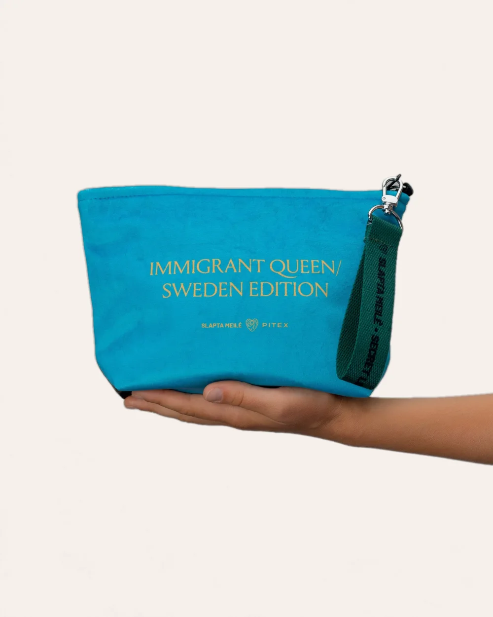 Mėlynos kosmetinės „IMMIGRANT QUEEN: Sweden Edition“ nugarėlė su auksiniu užrašu ant delno