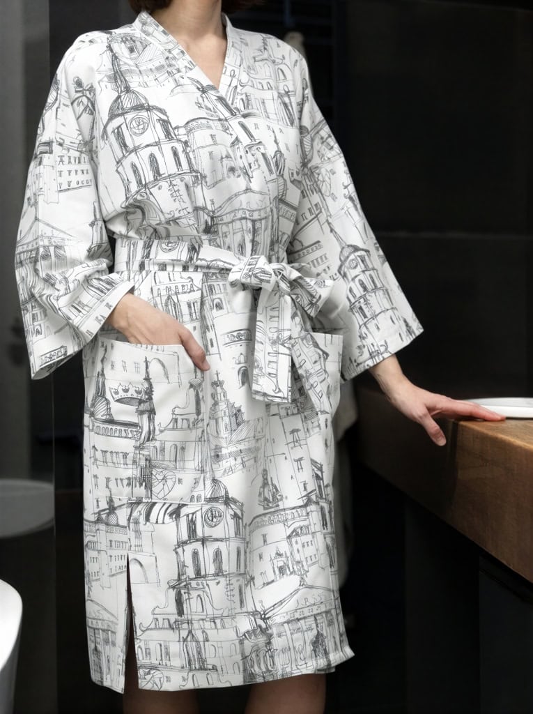 Modelė baltu chalatu kimono „Karališko Vilniaus meilės istorija“ vonioje prie stalviršio, priekis