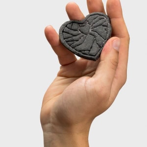 Tamsus reljefinis magnetukas „Karūnuota širdis širdyje“ laikomas pakeltoje rankoje