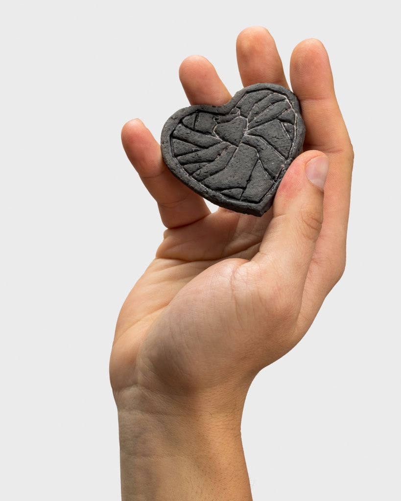 Tamsus reljefinis magnetukas „Karūnuota širdis širdyje“ laikomas pakeltoje rankoje