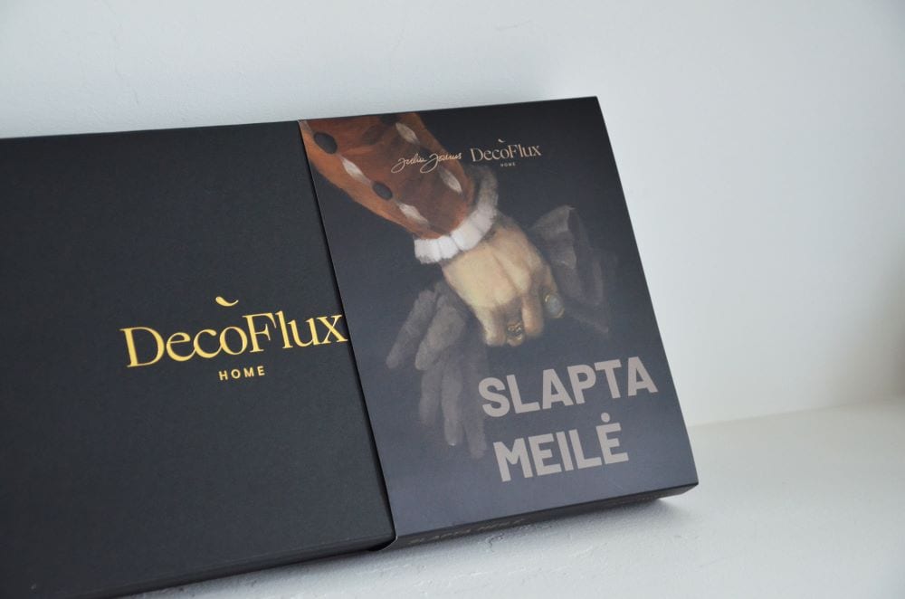Uždaryta juoda „DecoFlux“ dovanų dėžė su pilkais užvalkalais „Slapta Meilė“ ir paveikslo fragmentu