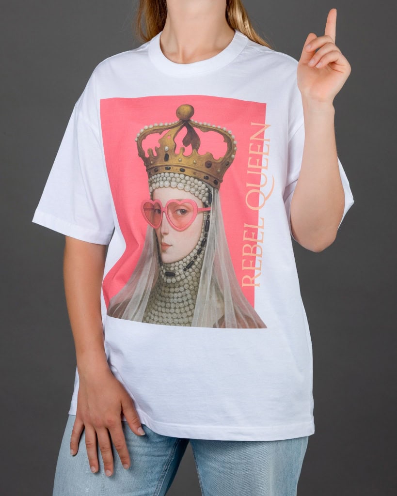 Moteris su baltais marškinėliais „REBEL QUEEN“ pakėlusi pirštą aukštyn