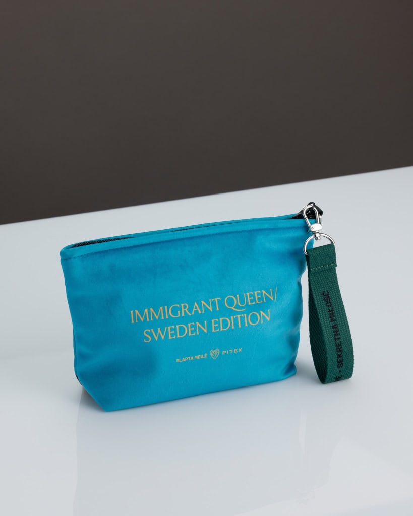 Mėlyna kosmetinė „IMMIGRANT QUEEN: Sweden Edition“ ant stalo, matoma pusė su auksiniu užrašu