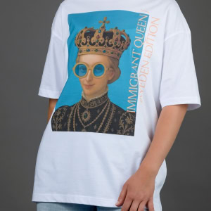 Moteris su baltais marškinėliais „IMIGRANT QUEEN / SWEDEN EDITION“, rankos nuleistos