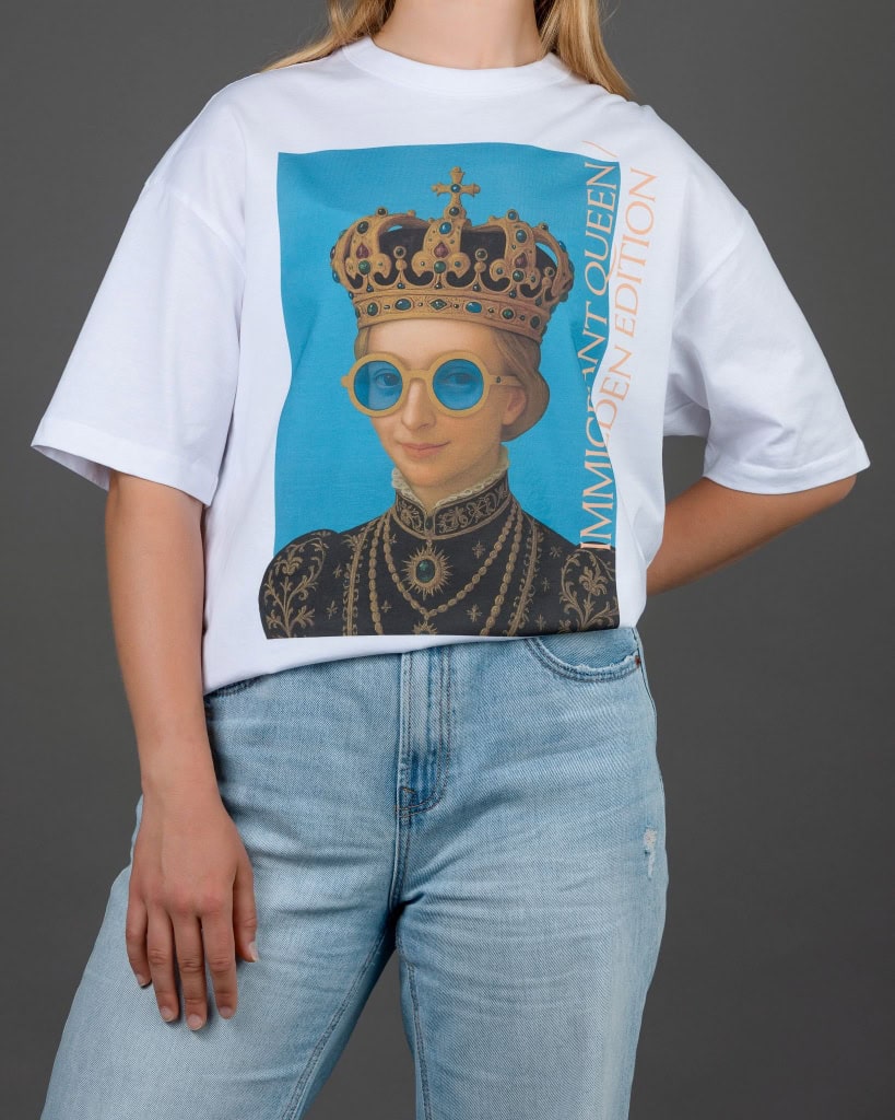 Moteris su baltais marškinėliais „IMIGRANT QUEEN / SWEDEN EDITION“, ranka už nugaros