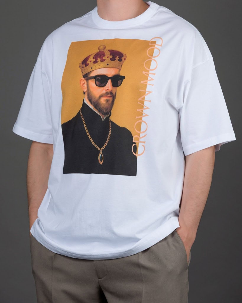 Vyras su baltais laisvo kirpimo marškinėliais „CROWN MOOD“ ir pilkomis kelnėmis