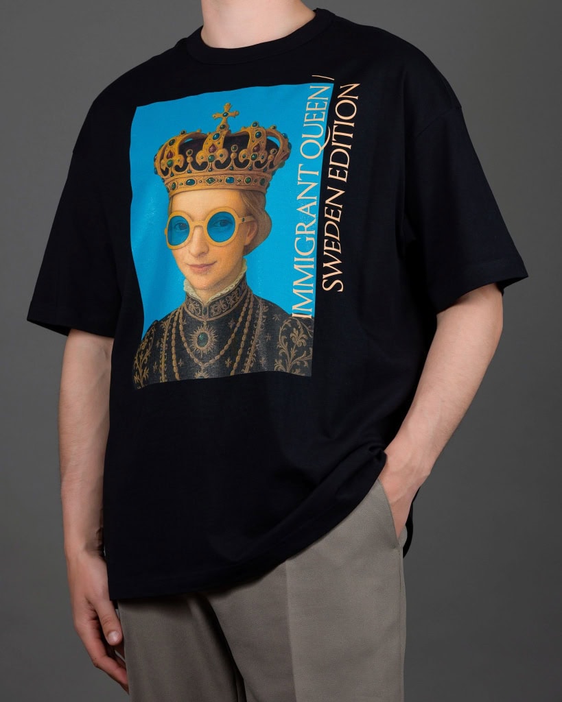 Vyras su juodais marškinėliais „IMIGRANT QUEEN / SWEDEN EDITION“, ranka kišenėje