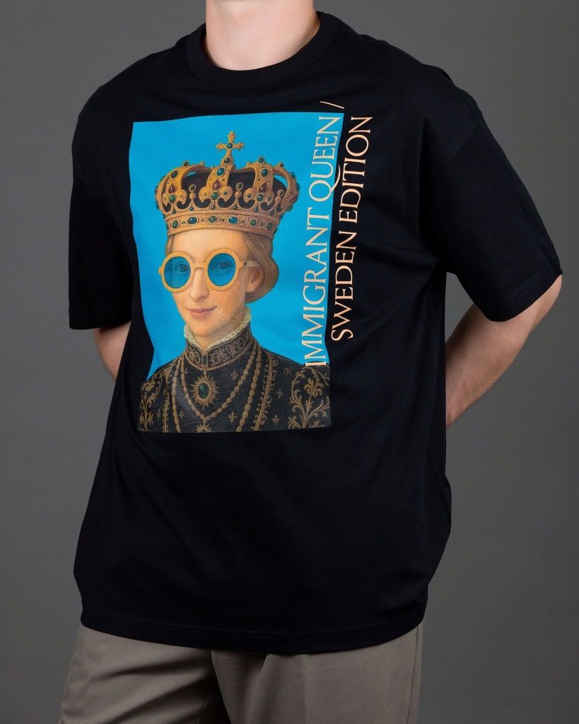 Vyras su juodais marškinėliais „IMIGRANT QUEEN / SWEDEN EDITION“, rankos už nugaros