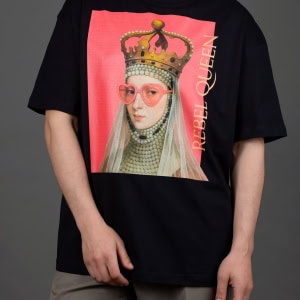 Vyras su juodais marškinėliais „REBEL QUEEN“ ir pilkomis kelnėmis, rankos nuleistos