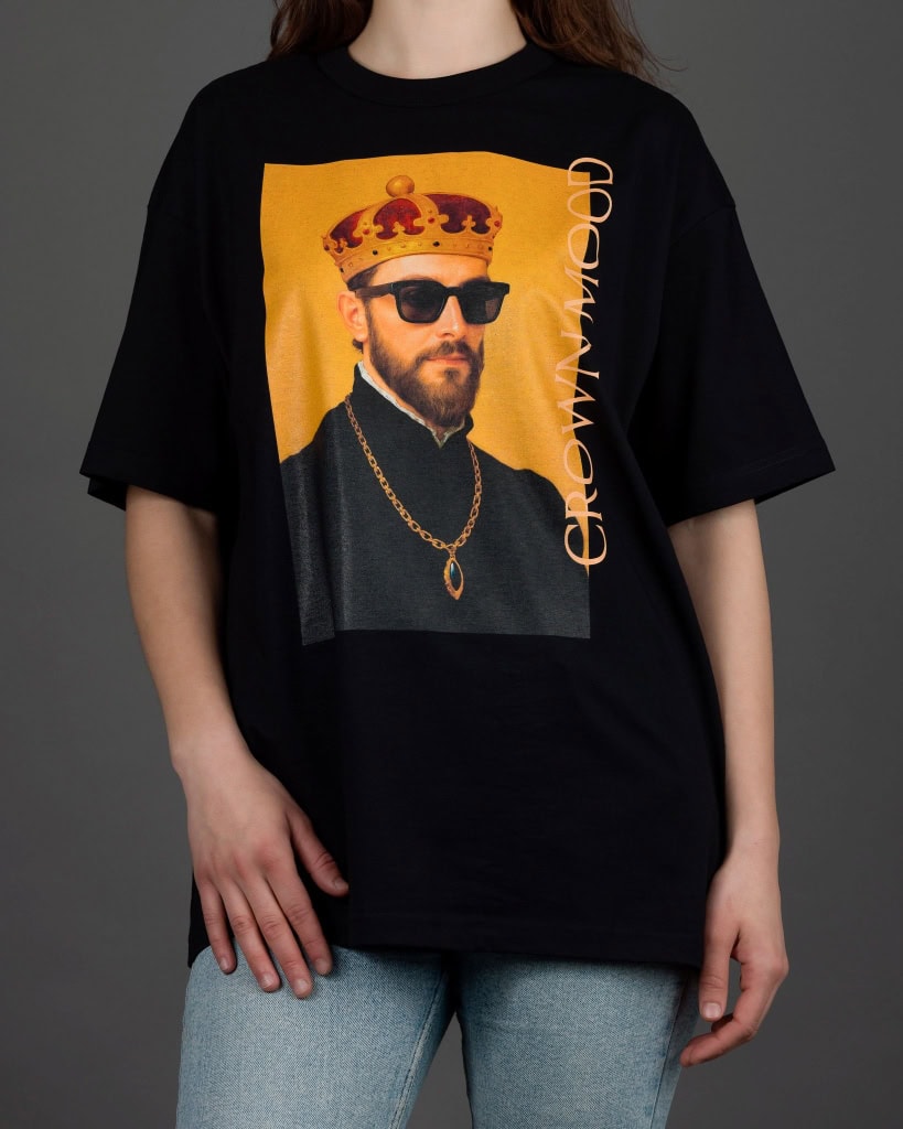 Moteris su juodais marškinėliais „CROWN MOOD“ ir šviesiais džinsais iš priekio