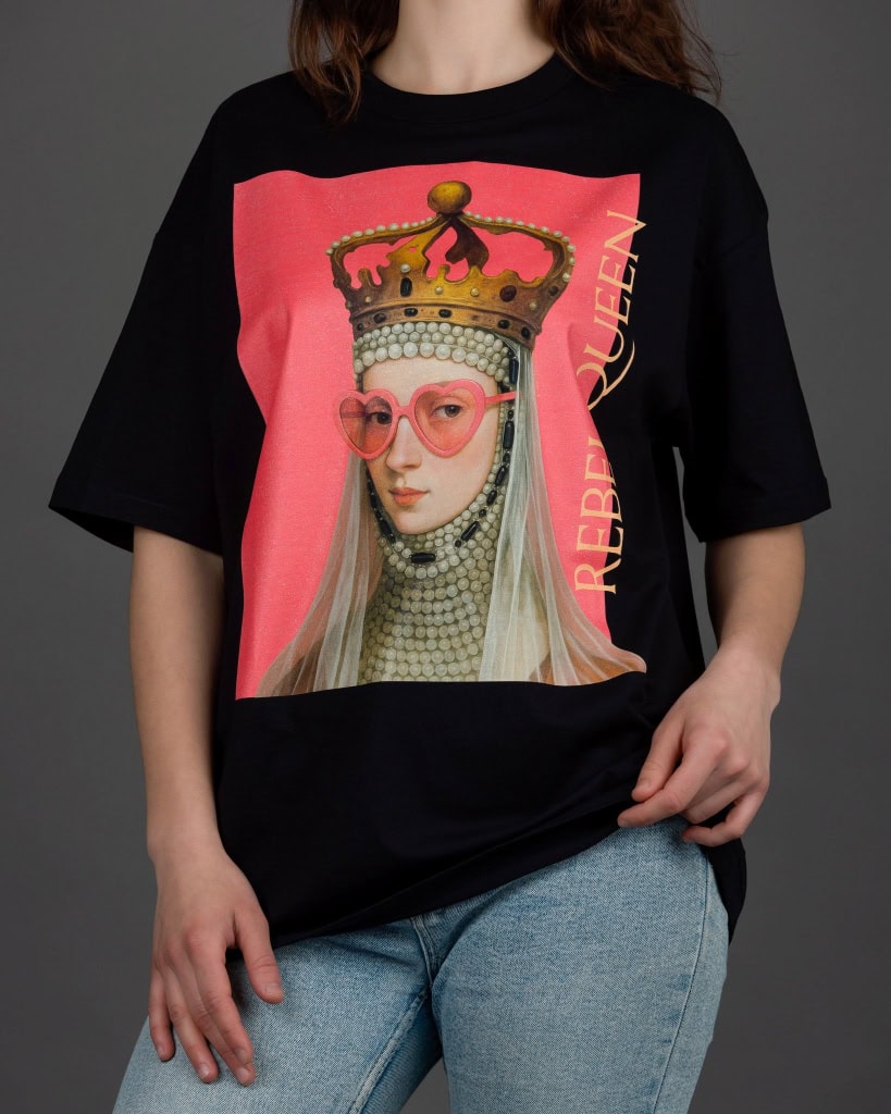 Moteris su juodais marškinėliais „REBEL QUEEN“ ir džinsais, rankos nuleistos