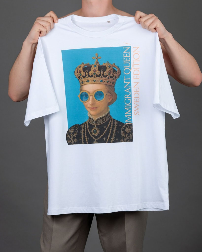 Vyras laiko iškėlęs baltus marškinėlius „IMIGRANT QUEEN / SWEDEN EDITION“ prieš save