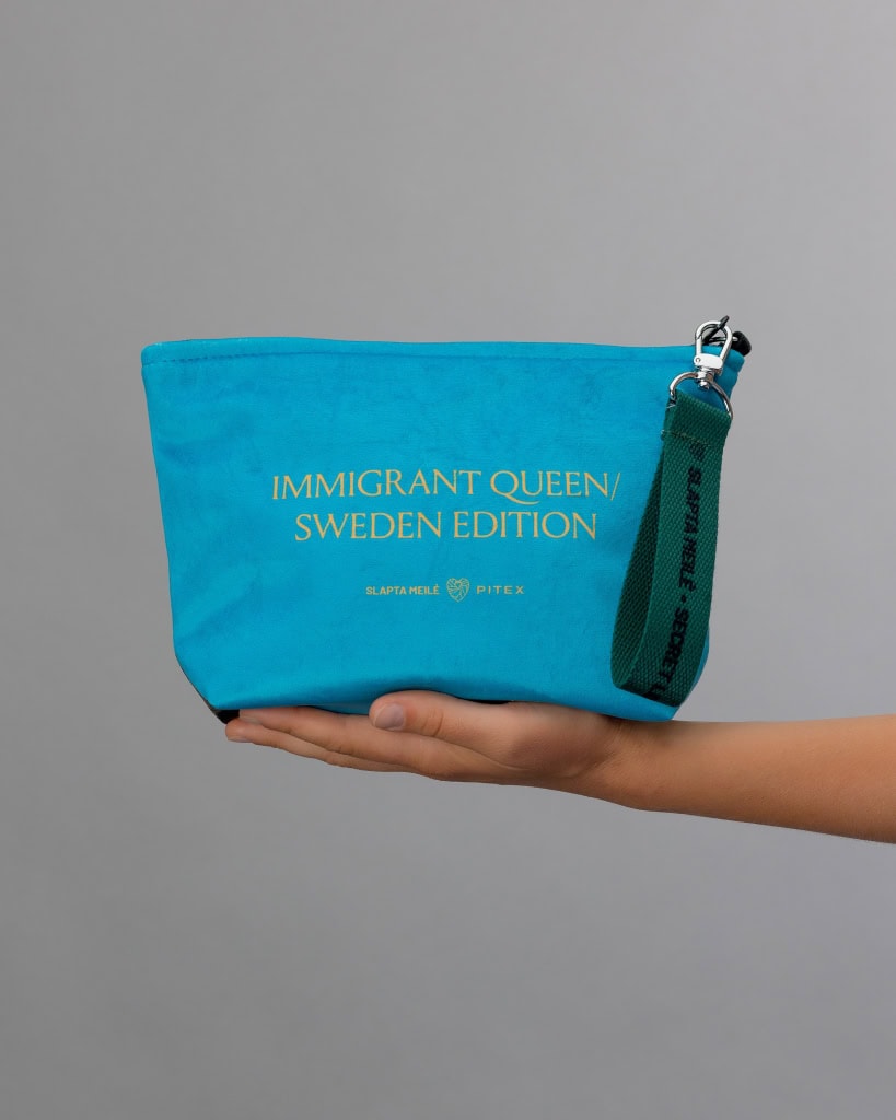 Mėlynos kosmetinės „IMMIGRANT QUEEN: Sweden Edition“ nugarėlė su auksiniu užrašu ant delno