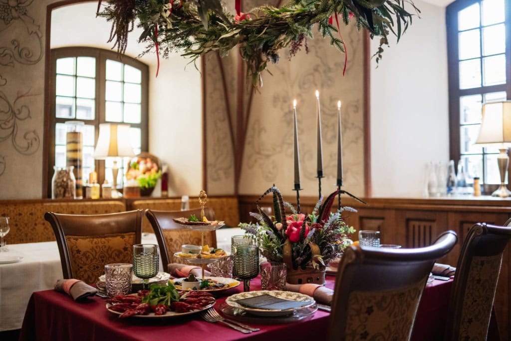 Restorano „Lokys“ salė su serviruotu stalu, aukštomis žvakėmis ir gėlių kompozicija