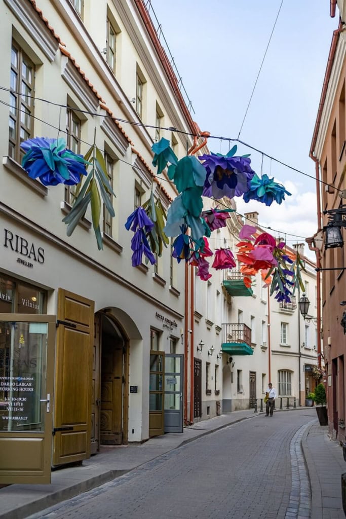 Siaura Vilniaus senamiesčio gatvelė su virš jos kabančiomis spalvotomis dekoracijomis