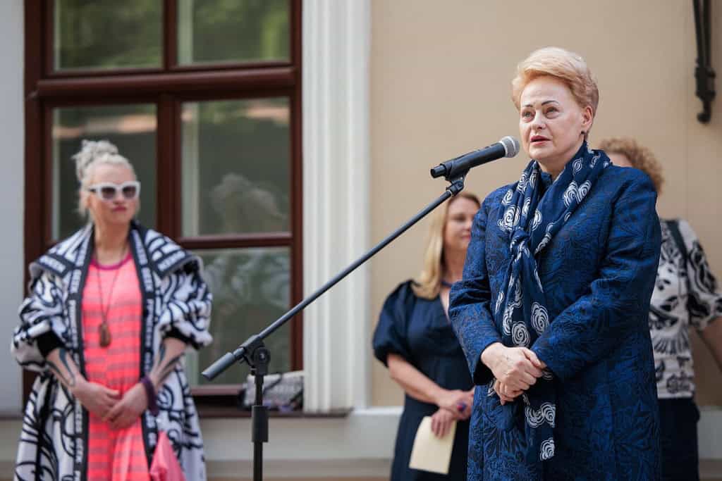 Parodos atidarymas: moteris kalba prie mikrofono, šalia stovi kalbos laukiantys svečiai