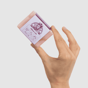 Ranka laiko rausvą kieto muilo „Šilkinė rožė“ 100 g gabalą su etikete, vaizdas kampu
