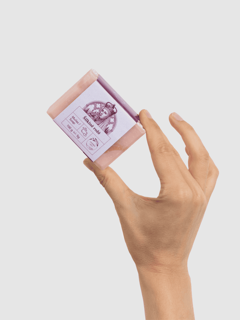 Ranka laiko rausvą kieto muilo „Šilkinė rožė“ 100 g gabalą su etikete, vaizdas kampu