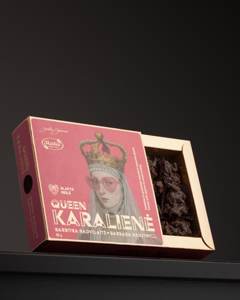 Atidaryta rožinė šokolado dėžutė „Queen Karalienė“ su karalienės portretu ant tamsios lentynos