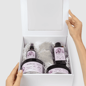 Atidaryta balta dovanų dėžė „Karališkas SPA“ su levandų produktais, laikoma rankomis