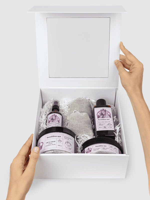 Atidaryta balta dovanų dėžė „Karališkas SPA“ su levandų produktais, laikoma rankomis