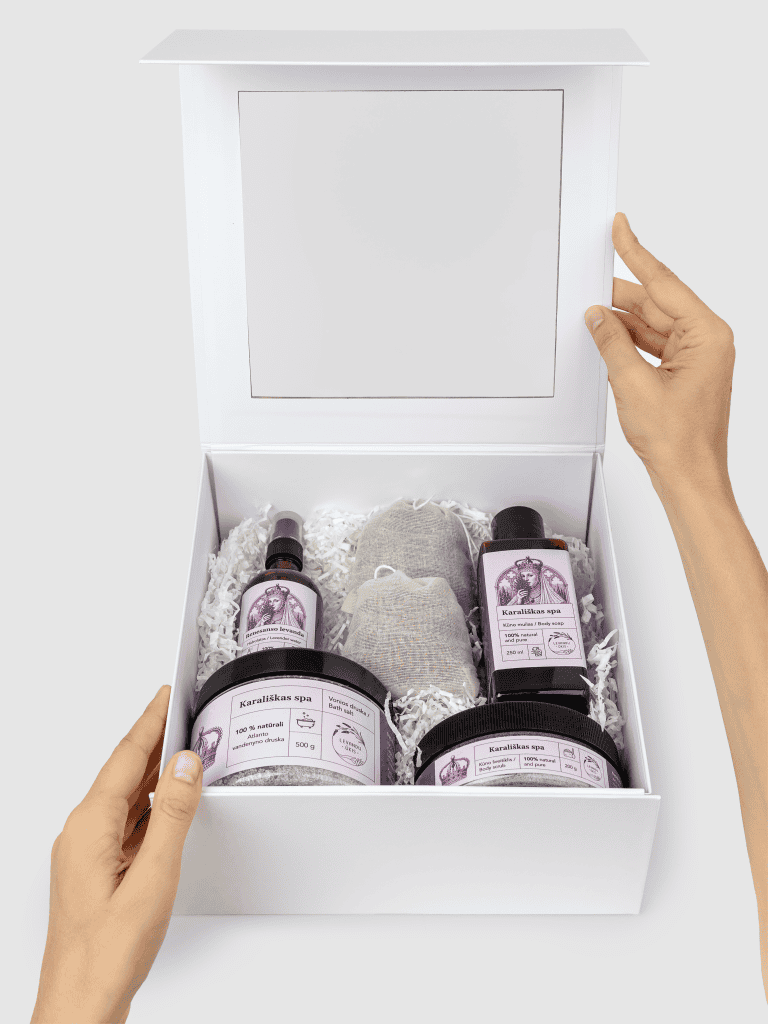 Atidaryta balta dovanų dėžė „Karališkas SPA“ su levandų produktais, laikoma rankomis